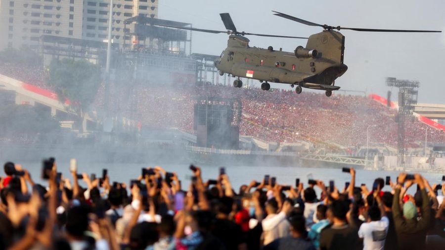 Penonton bersorak saat helikopter Chinook Angkatan Udara Singapura dikawal oleh helikopter Apache berparade dengan bendera Singapura untuk menandai Hari Nasional ke-57 negara itu, di Singapura, Selasa (9/8/2022). (Photo by ROSLAN RAHMAN/AFP via Getty Images)