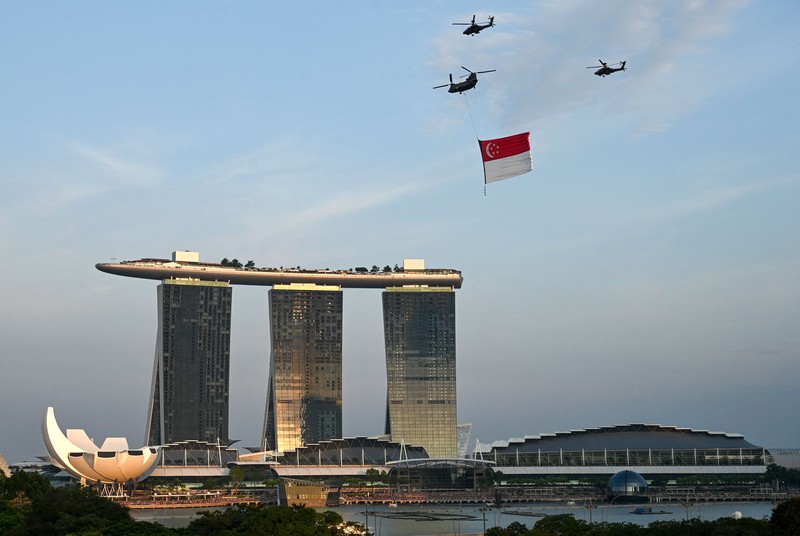 Perayaan Hari Nasional di Singapura Penonton bersorak saat helikopter Chinook Angkatan Udara Singapura dikawal oleh helikopter Apache berparade dengan bendera Singapura untuk menandai Hari Nasional ke-57 negara itu, di Singapura, Selasa (9/8/2022). (Photo by ROSLAN RAHMAN/AFP via Getty Images)
