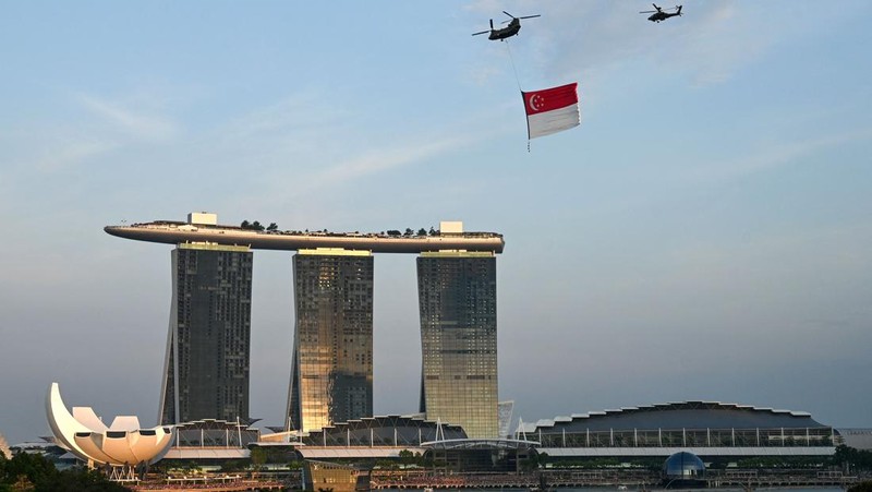 Penonton bersorak saat helikopter Chinook Angkatan Udara Singapura dikawal oleh helikopter Apache berparade dengan bendera Singapura untuk menandai Hari Nasional ke-57 negara itu, di Singapura, Selasa (9/8/2022). (Photo by ROSLAN RAHMAN/AFP via Getty Images)