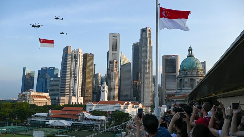 Penonton bersorak saat helikopter Chinook Angkatan Udara Singapura dikawal oleh helikopter Apache berparade dengan bendera Singapura untuk menandai Hari Nasional ke-57 negara itu, di Singapura, Selasa (9/8/2022). (Photo by ROSLAN RAHMAN/AFP via Getty Images)