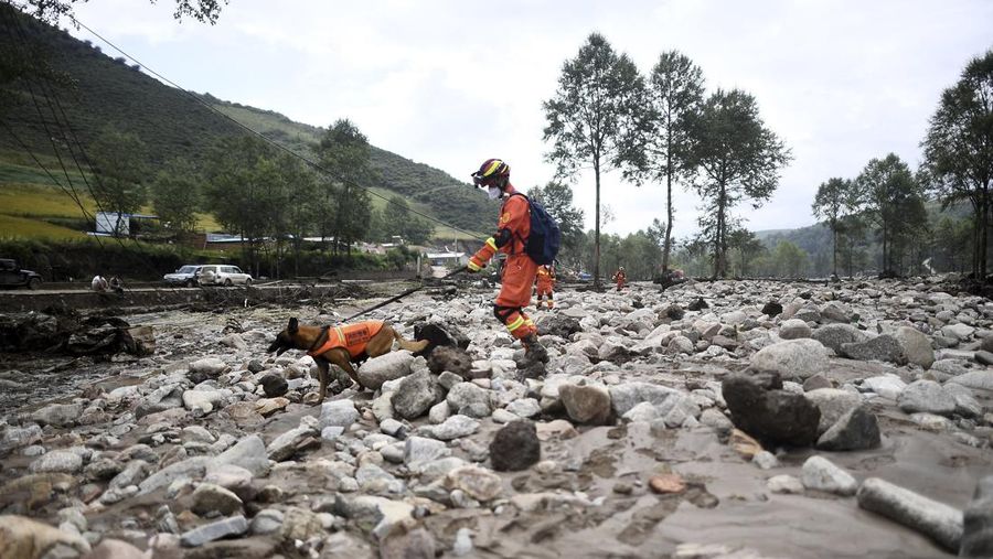 Seorang pekerja penyelamat dan anjing mencari korban setelah banjir di Desa Shadai, Kotapraja Qingshan di Datong Hui dan Kabupaten Otonom Tu di Provinsi Qinghai, Tiongkok barat laut, Kamis (18/8/2022). Badai hujan yang melanda Tiongkok barat memicu tanah longsor yang mengalihkan sungai dan menyebabkan banjir bandang di daerah berpenduduk, menewaskan beberapa orang dan membuat yang lain hilang.  (Zhang Hongxiang/Xinhua via AP)