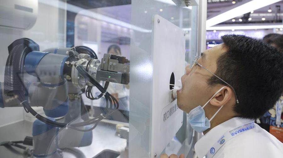 BEIJING, CHINA - AUGUST 18: A staff member takes part in a demonstration of a robot arm collecting swab samples for coronavirus disease (COVID-19) detection during the 2022 World Robot Conference at Beijing Etrong International Exhibition on August 18, 2022 in Beijing, China. The 2022 World Robot Conference kicked off on Thursday in Beijing. (Photo by Lintao Zhang/Getty Images)