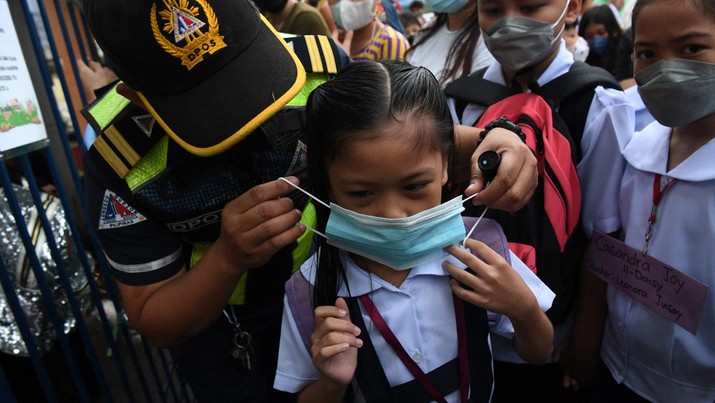 1242648063 A city hall employee helps a student put on a face mask during the opening of classes at a school in Quezon City, suburban Manila on August 22, 2022 as millions of children in the Philippines returned to school as the academic year started on August 22, with many taking their seats in classrooms for the first time since the Covid-19 pandemic hit. (Photo by Ted ALJIBE / AFP) (Photo by TED ALJIBE/AFP via Getty Images)