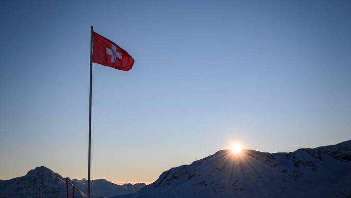 This photograph shows a Swiss flag floating at sunrise in a landscape of snow covered mountains above the resort of St. Moritz on December 12, 2021 (Photo by Fabrice COFFRINI / AFP) (Photo by FABRICE COFFRINI/AFP via Getty Images)