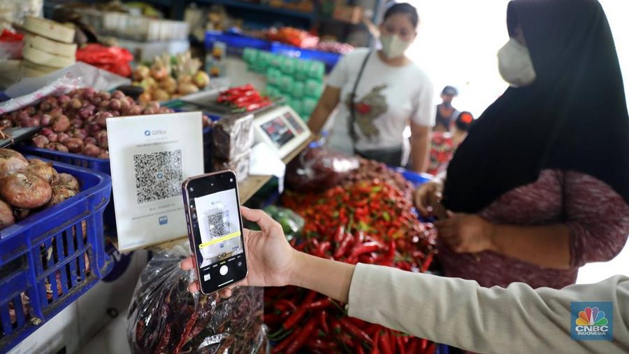 Pembeli membayar belanjaanya dengan menggunakan aplikasi pembayaran digital QRIS (QR Code Indonesian Standard) untuk transaksi dagang di pasar Badung, Denpasar, Bali, Selasa, (30/8/2022). (CNBC Indonesia/Muhammad Sabki)