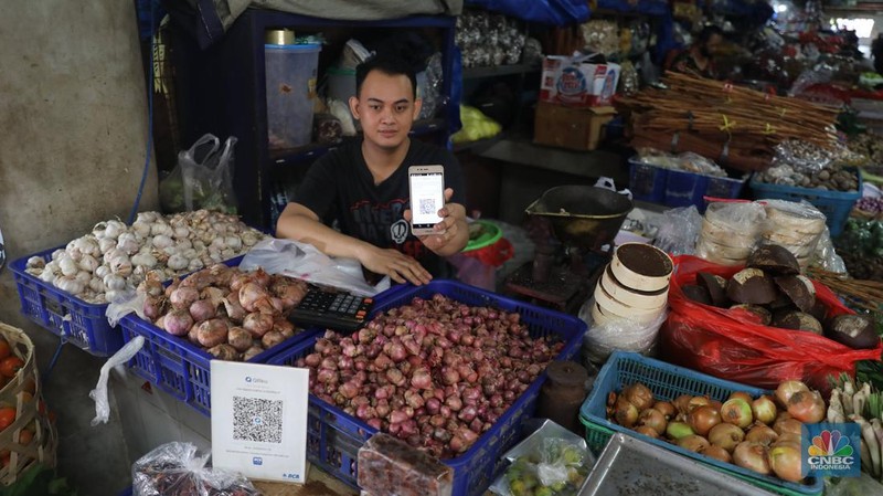 Pembeli membayar belanjaanya dengan menggunakan aplikasi pembayaran digital QRIS (QR Code Indonesian Standard) untuk transaksi dagang di pasar Badung, Denpasar, Bali, Selasa, (30/8/2022). (CNBC Indonesia/Muhammad Sabki)