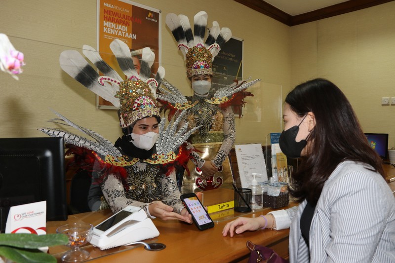 Petugas Customer Service Bank Mega memakai kostum adat Suku Dayak saat memberikan pelayanan m banking kepada salah seorang nasabah di KCP Jakarta Cinere, Kota Depok, Jawa Barat, Senin (5/9/2022). Sehubungan dengan pelaksanaan Hari Pelanggan Nasional, karyawan Bank Mega di seluruh Kantor Cabang dan Kantor Cabang Pembantu sengaja memakai kostum dengan beragam tema guna memberikan pengalaman yang berbeda kepada para nasabah yang berkunjung. (Dok. Bank Mega)