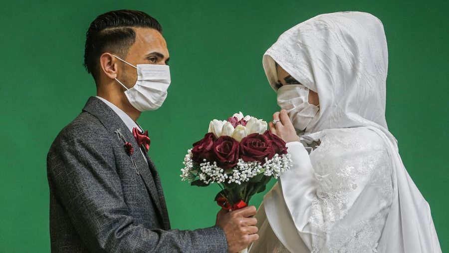 Palestinian groom Mohamed abu Daga and his bride Israa wear protective masks amid the COVID-19 epidemic, during a photoshoot at a studio before their wedding ceremony in Khan Yunis in the southern Gaza Strip, on March 23, 2020. - Authorities in Gaza confirmed on March 22 the first two cases of novel coronavirus, identifying them as Palestinians who had travelled to Pakistan and were being held in quarantine since their return, as the United Nations warned of potential disastrous outcomes to an outbreak given the high poverty rates and weak health system in the coastal strip, under Israeli blockade since 2007. (Photo by SAID KHATIB / AFP) (Photo by SAID KHATIB/AFP via Getty Images)