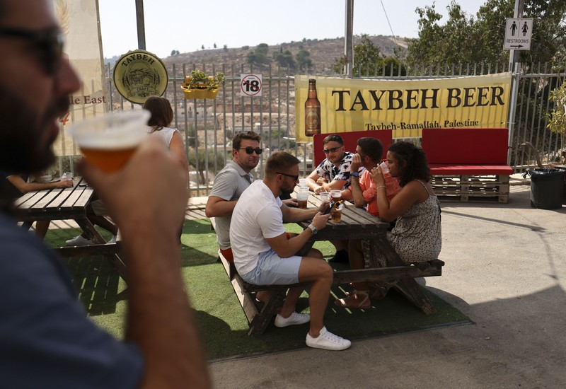 Seorang bartender melayani pengunjung pada festival bir tahunan Oktoberfest di desa Taybeh di desa Taybeh, sebelah timur kota Ramallah Tepi Barat, Palestina, Jumat (2/92/2022). Bir Taybeh dibuat dari buah anggur yang tumbuh di kebun anggur dekat Kota Birzeit, West Bank, sekitar 10 kilometer timur laut Ramallah. Bir Taybeh diseduh dalam jumlah kecil, tanpa menggunakan bahan pengawet atau gula tambahan. Taybeh Brewing Company didirikan oleh Nadim Khoury dan keluarganya pada 1994 di West Bank, Palestina dan kini diteruskan oleh seorang wanita bernama Madees Khoury, (Photo by ABBAS MOMANI/AFP via Getty Images).