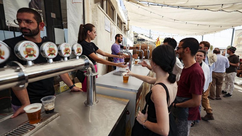 Seorang bartender melayani pengunjung pada festival bir tahunan Oktoberfest di desa Taybeh di desa Taybeh, sebelah timur kota Ramallah Tepi Barat, Palestina, Jumat (2/92/2022). Bir Taybeh dibuat dari buah anggur yang tumbuh di kebun anggur dekat Kota Birzeit, West Bank, sekitar 10 kilometer timur laut Ramallah. Bir Taybeh diseduh dalam jumlah kecil, tanpa menggunakan bahan pengawet atau gula tambahan. Taybeh Brewing Company didirikan oleh Nadim Khoury dan keluarganya pada 1994 di West Bank, Palestina dan kini diteruskan oleh seorang wanita bernama Madees Khoury, (Photo by ABBAS MOMANI/AFP via Getty Images).