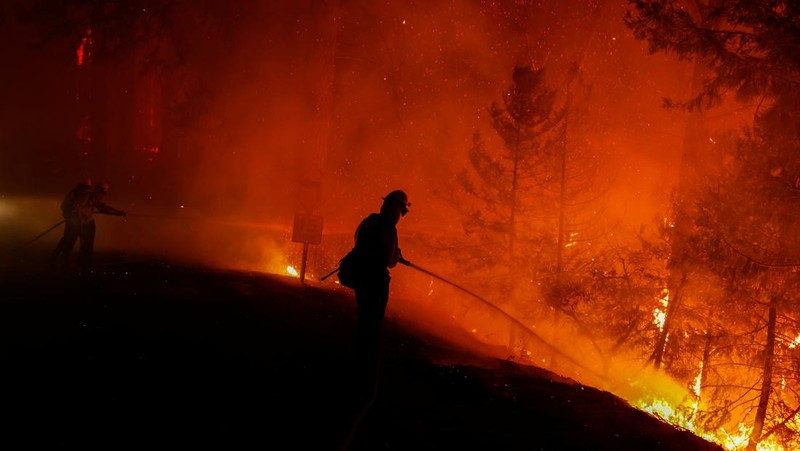 Sebuah pesawat pemadam kebakaran bekerja memadamkan api yang telah mendekati rumah selama Kebakaran hutan Fairview dekat Hemet, California di Riverside County, AS, Rabu (7/9/2022). Kebakaran hutan akibat gelombang panas di California, Amerika Serikat (AS), terus meluas dengan cepat. Kejadian tersebut menyebabkan dua orang tewas dan ribuan orang dievakuasi untuk mengungsi.  (Photo by PATRICK T. FALLON/AFP via Getty Images)