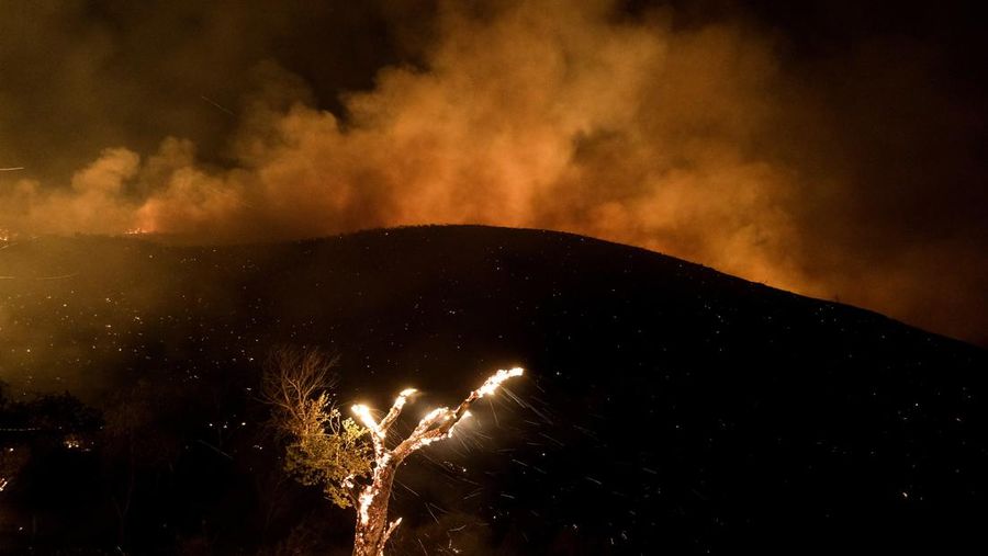 Sebuah pesawat pemadam kebakaran bekerja memadamkan api yang telah mendekati rumah selama Kebakaran hutan Fairview dekat Hemet, California di Riverside County, AS, Rabu (7/9/2022). Kebakaran hutan akibat gelombang panas di California, Amerika Serikat (AS), terus meluas dengan cepat. Kejadian tersebut menyebabkan dua orang tewas dan ribuan orang dievakuasi untuk mengungsi.  (Photo by PATRICK T. FALLON/AFP via Getty Images)