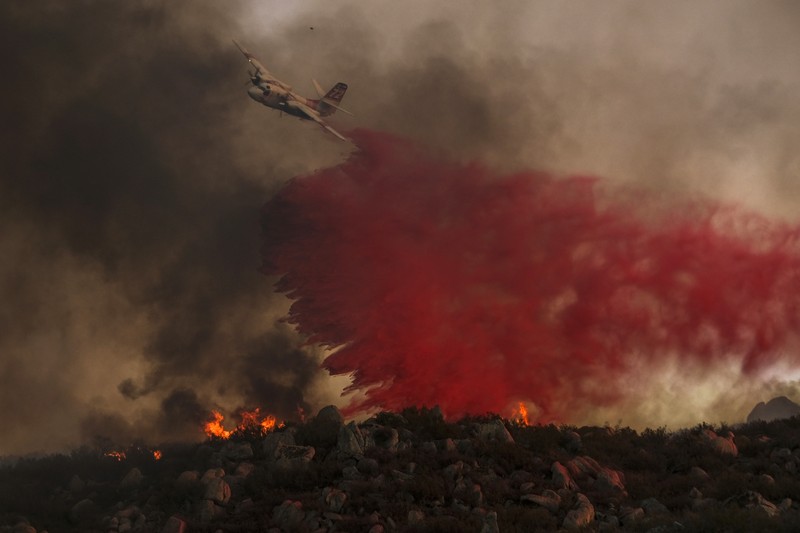 Sebuah pesawat pemadam kebakaran bekerja memadamkan api yang telah mendekati rumah selama Kebakaran hutan Fairview dekat Hemet, California di Riverside County, AS, Rabu (7/9/2022). Kebakaran hutan akibat gelombang panas di California, Amerika Serikat (AS), terus meluas dengan cepat. Kejadian tersebut menyebabkan dua orang tewas dan ribuan orang dievakuasi untuk mengungsi.  (Photo by PATRICK T. FALLON/AFP via Getty Images)