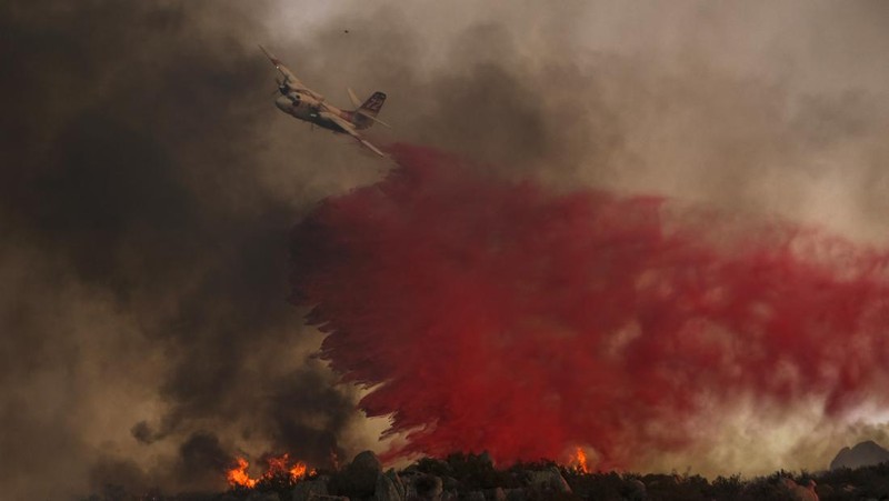 Sebuah pesawat pemadam kebakaran bekerja memadamkan api yang telah mendekati rumah selama Kebakaran hutan Fairview dekat Hemet, California di Riverside County, AS, Rabu (7/9/2022). Kebakaran hutan akibat gelombang panas di California, Amerika Serikat (AS), terus meluas dengan cepat. Kejadian tersebut menyebabkan dua orang tewas dan ribuan orang dievakuasi untuk mengungsi.  (Photo by PATRICK T. FALLON/AFP via Getty Images)