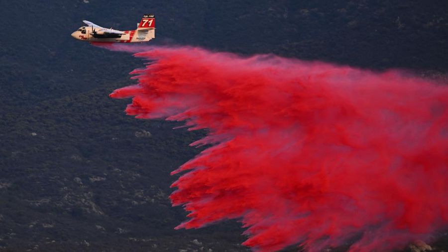 Sebuah pesawat pemadam kebakaran bekerja memadamkan api yang telah mendekati rumah selama Kebakaran hutan Fairview dekat Hemet, California di Riverside County, AS, Rabu (7/9/2022). Kebakaran hutan akibat gelombang panas di California, Amerika Serikat (AS), terus meluas dengan cepat. Kejadian tersebut menyebabkan dua orang tewas dan ribuan orang dievakuasi untuk mengungsi.  (Photo by PATRICK T. FALLON/AFP via Getty Images)