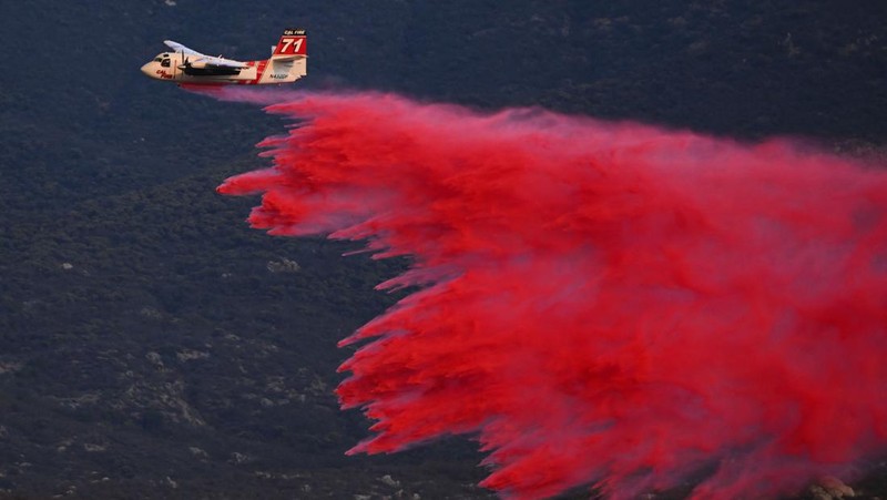 Sebuah pesawat pemadam kebakaran bekerja memadamkan api yang telah mendekati rumah selama Kebakaran hutan Fairview dekat Hemet, California di Riverside County, AS, Rabu (7/9/2022). Kebakaran hutan akibat gelombang panas di California, Amerika Serikat (AS), terus meluas dengan cepat. Kejadian tersebut menyebabkan dua orang tewas dan ribuan orang dievakuasi untuk mengungsi.  (Photo by PATRICK T. FALLON/AFP via Getty Images)