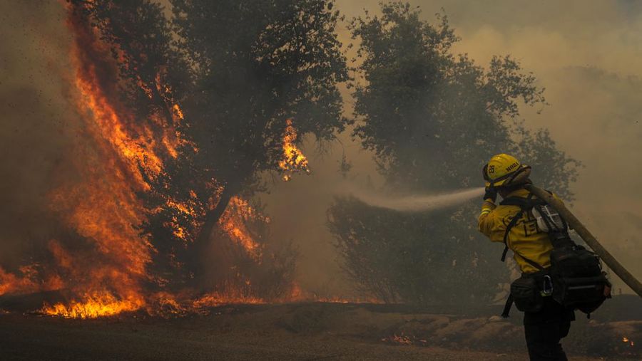 Sebuah pesawat pemadam kebakaran bekerja memadamkan api yang telah mendekati rumah selama Kebakaran hutan Fairview dekat Hemet, California di Riverside County, AS, Rabu (7/9/2022). Kebakaran hutan akibat gelombang panas di California, Amerika Serikat (AS), terus meluas dengan cepat. Kejadian tersebut menyebabkan dua orang tewas dan ribuan orang dievakuasi untuk mengungsi.  (Photo by PATRICK T. FALLON/AFP via Getty Images)