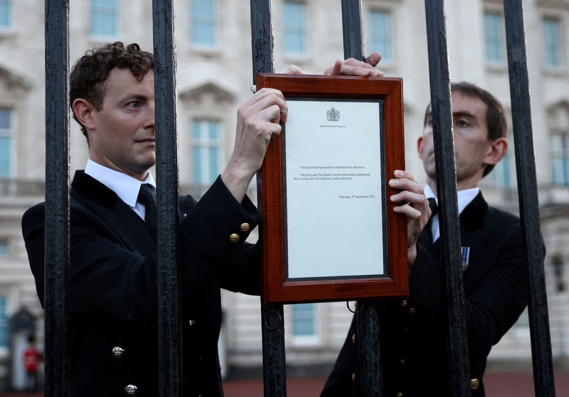Pengumuman meninggalnya Ratu Elizabeth di pagar di luar Istana Buckingham, London, Inggris Personil menempatkan tanda yang mengumumkan meninggalnya Ratu Elizabeth di pagar di luar Istana Buckingham, London, Inggris, Kamis (8/9/2022). Ratu Elizabeth yang merupakan raja terlama yang memerintah Inggris dan tokoh negara selama tujuh dekade meninggal dalam usia 96 tahun.( REUTERS/Henry Nicholls)