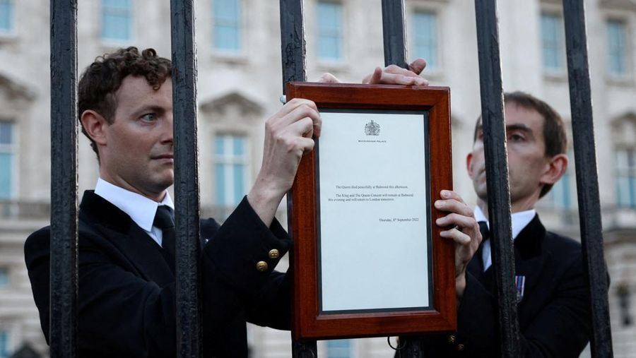 Personil menempatkan tanda yang mengumumkan meninggalnya Ratu Elizabeth di pagar di luar Istana Buckingham, London, Inggris, Kamis (8/9/2022). Ratu Elizabeth yang merupakan raja terlama yang memerintah Inggris dan tokoh negara selama tujuh dekade meninggal dalam usia 96 tahun.( REUTERS/Henry Nicholls)