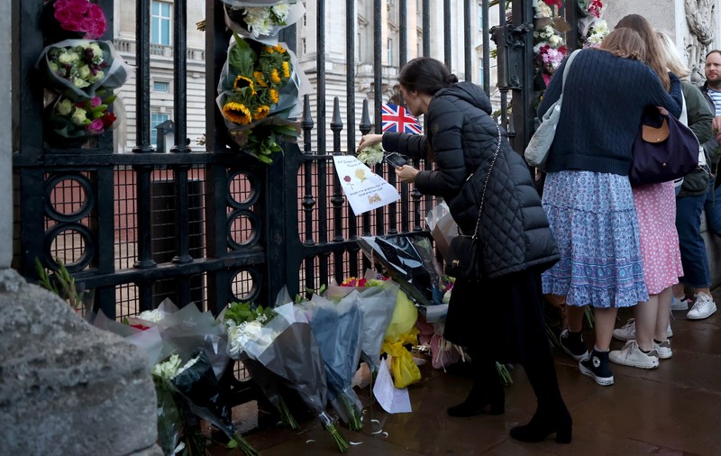 Personil menempatkan tanda yang mengumumkan meninggalnya Ratu Elizabeth di pagar di luar Istana Buckingham, London, Inggris, Kamis (8/9/2022). Ratu Elizabeth yang merupakan raja terlama yang memerintah Inggris dan tokoh negara selama tujuh dekade meninggal dalam usia 96 tahun.( REUTERS/Henry Nicholls)
