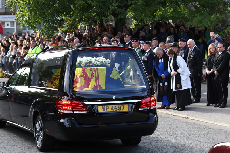 Mobil jenazah yang membawa peti mati Ratu Elizabeth Inggris meninggalkan Kastil Balmoral, di Balmoral, Skotlandia, Inggris ke Istana Holyroodhouse di Edinburgh Mobil jenazah membawa peti mati Ratu Elizabeth II yang ditutupi Standar Kerajaan untuk Skotlandia dan karangan bunga meninggalkan Kastil Balmoral, di Balmoral, Skotlandia, Inggris, Minggu (11/9/2022). Peti mati ratu akan dibawa sejauh 290 km melalui jalan darat dari perkebunan terpencil ke Istana Holyroodhouse di Edinburgh. (Photo by Owen Humphreys/PA Images via Getty Images)