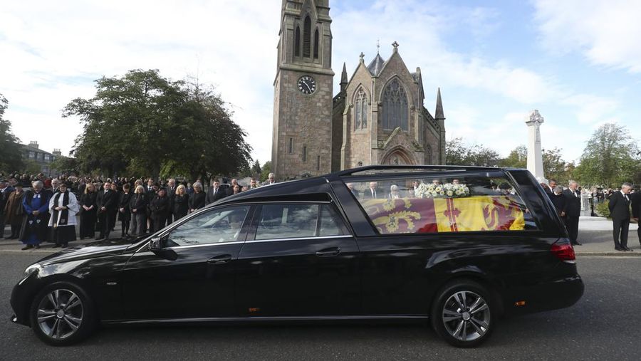 Orang-orang berbaris saat mobil jenazah yang membawa peti mati Ratu Elizabeth II melewati desa Ballater, dekat Balmoral, Skotlandia, Inggris, Minggu (11/9/2022). Peti mati ratu akan dibawa sejauh 290 km melalui jalan darat dari perkebunan terpencil ke Istana Holyroodhouse di Edinburgh. (AP Photo/Scott Heppell)