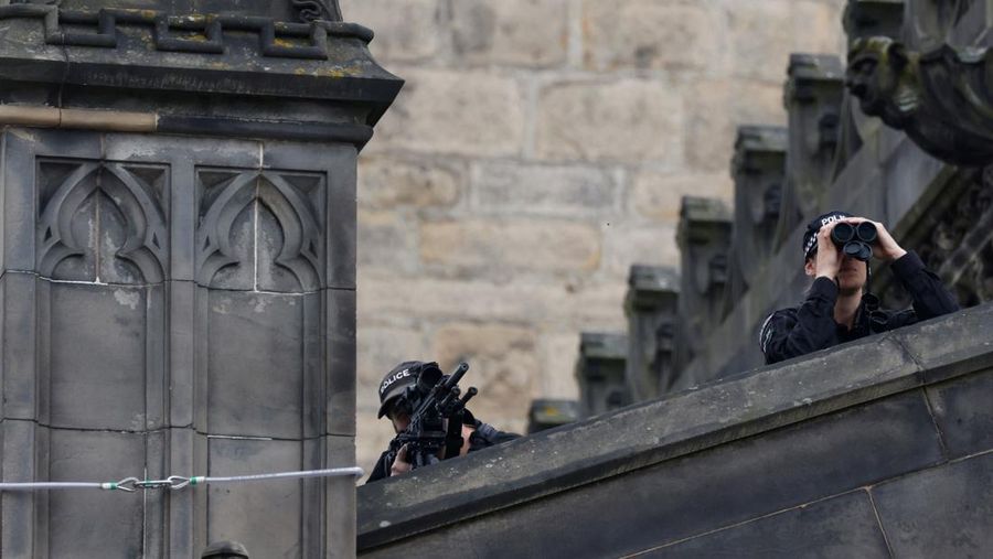 Police officers with snipers stand on the roof of the St Giles' Cathedral in Edinburgh on September 11, 2022, where Queen Elizabeth II will lie at rest and ahead of the ceremony of the proclamation of Britain's King Charles III. - Queen Elizabeth II's coffin will travel by road through Scottish towns and villages on Sunday as it begins its final journey from her beloved Scottish retreat of Balmoral. The Queen, who died on September 8, will be taken to the Palace of Holyroodhouse before lying at rest in St Giles' Cathedral, before travelling onwards to London for her funeral. (Photo by Oli SCARFF / AFP) (Photo by OLI SCARFF/AFP via Getty Images)