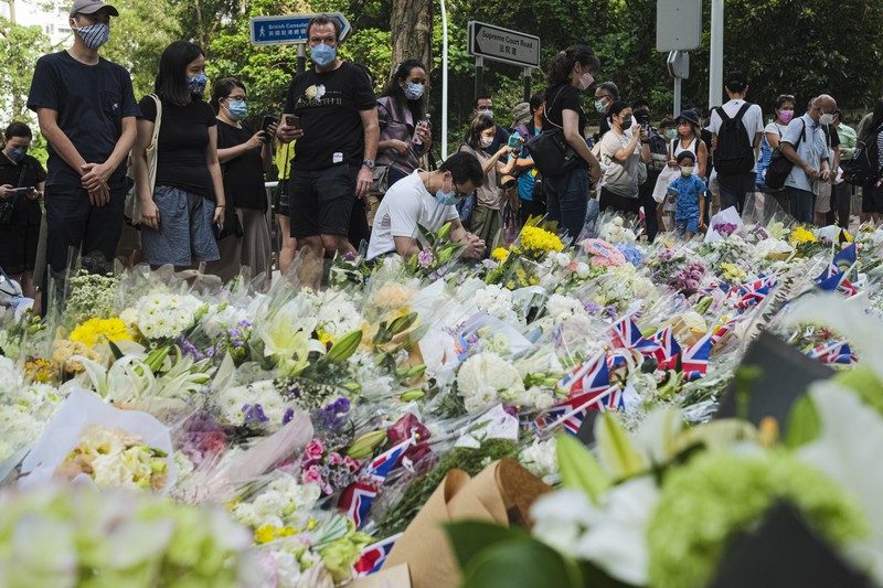 People queue to sign a condolence book next to flowers placed as a tribute outside the British Consulate in Hong Kong on September 12, 2022, following the death of Britain's Queen Elizabeth II. (Photo by Peter PARKS / AFP) (Photo by PETER PARKS/AFP via Getty Images)