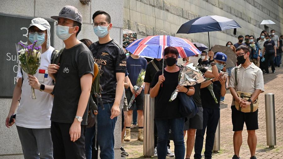 People queue to sign a condolence book next to flowers placed as a tribute outside the British Consulate in Hong Kong on September 12, 2022, following the death of Britain's Queen Elizabeth II. (Photo by Peter PARKS / AFP) (Photo by PETER PARKS/AFP via Getty Images)