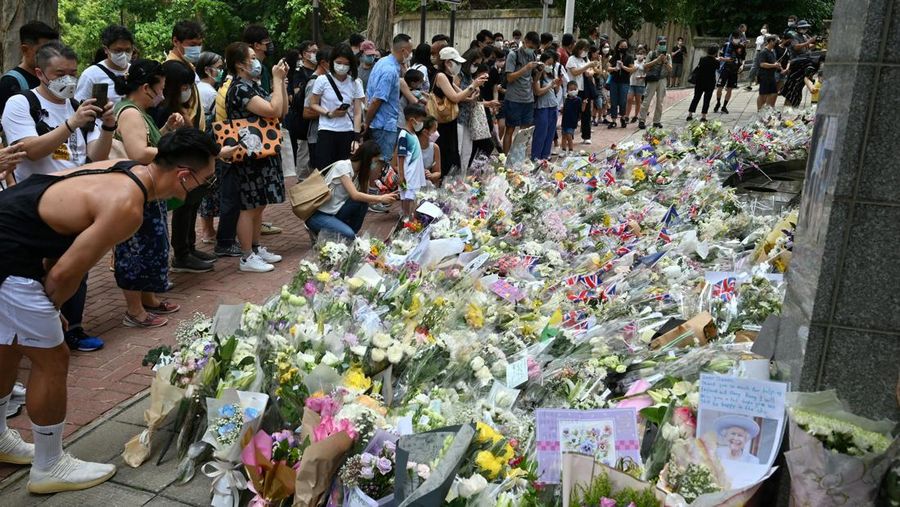 People queue to sign a condolence book next to flowers placed as a tribute outside the British Consulate in Hong Kong on September 12, 2022, following the death of Britain's Queen Elizabeth II. (Photo by Peter PARKS / AFP) (Photo by PETER PARKS/AFP via Getty Images)