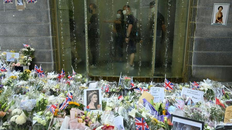 People queue to sign a condolence book next to flowers placed as a tribute outside the British Consulate in Hong Kong on September 12, 2022, following the death of Britain's Queen Elizabeth II. (Photo by Peter PARKS / AFP) (Photo by PETER PARKS/AFP via Getty Images)