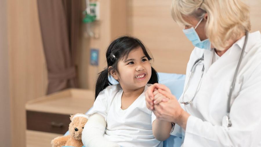 Young smiling female pediatrician doctor and child patient with teddy bear in the health medical center, talking positively with kid for the encouragement