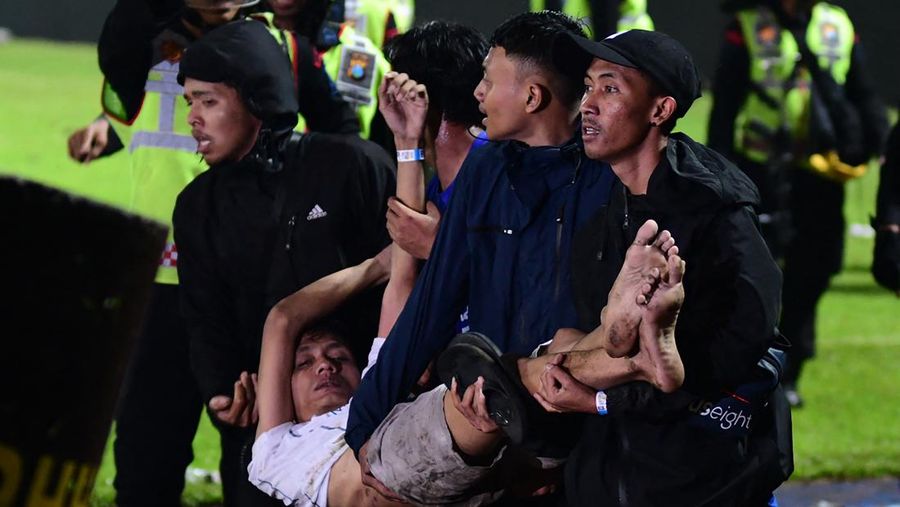 In this picture taken on October 1, 2022, a group of people carry a man after a football match between Arema FC and Persebaya Surabaya at Kanjuruhan stadium in Malang, East Java. - At least 127 people died at a football stadium in Indonesia late on October 1 when fans invaded the pitch and police responded with tear gas, triggering a stampede, officials said. (Photo by AFP) (Photo by STR/AFP via Getty Images)