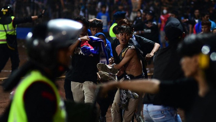 1243656587 In this picture taken on October 1, 2022, a group of people carry a man after a football match between Arema FC and Persebaya Surabaya at Kanjuruhan stadium in Malang, East Java. - At least 127 people died at a football stadium in Indonesia late on October 1 when fans invaded the pitch and police responded with tear gas, triggering a stampede, officials said. (Photo by AFP) (Photo by STR/AFP via Getty Images)