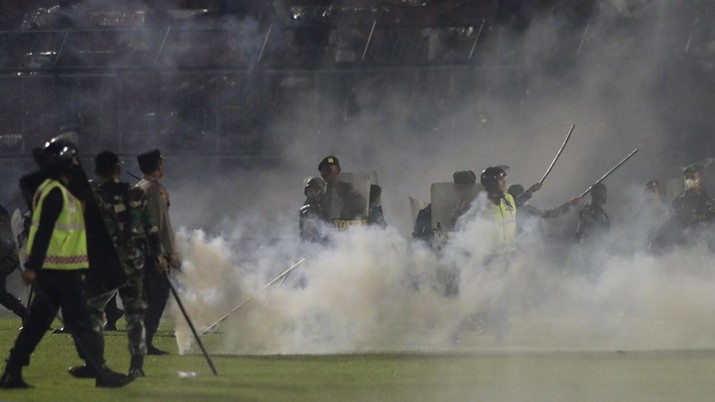 APTOPIX Indonesia Soccer Deaths Police officers and soldiers stand amid tear gas smoke after clashes between fans during a soccer match at Kanjuruhan Stadium in Malang, East Java, Indonesia, Saturday, Oct. 1, 2022. Panic following police actions left over 100 dead, mostly trampled to death, police said Sunday. (AP Photo/Yudha Prabowo)