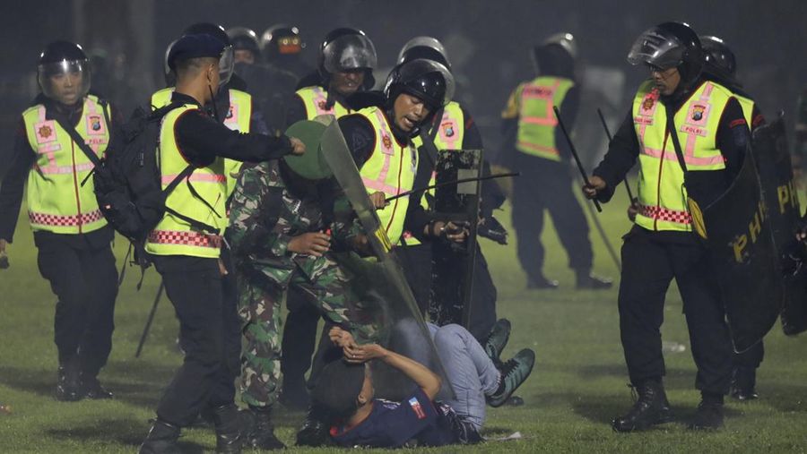 Plain-clothed officers stand near the wreckage of police vehicles damaged during a clash between supporters of two Indonesian soccer teams at Kanjuruhan Stadium in Malang, East Java, Indonesia, Saturday, Oct. 1, 2022. Panic following police actions left over 100 dead, mostly trampled to death, police said Sunday. (AP Photo/Yudha Prabowo)