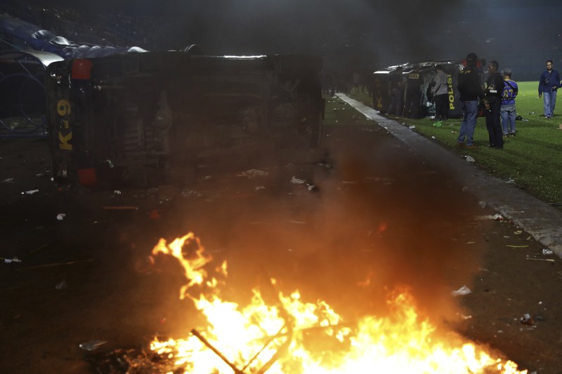 Indonesia Soccer Deaths Plain-clothed officers stand near the wreckage of police vehicles damaged during a clash between supporters of two Indonesian soccer teams at Kanjuruhan Stadium in Malang, East Java, Indonesia, Saturday, Oct. 1, 2022. Panic following police actions left over 100 dead, mostly trampled to death, police said Sunday. (AP Photo/Yudha Prabowo)