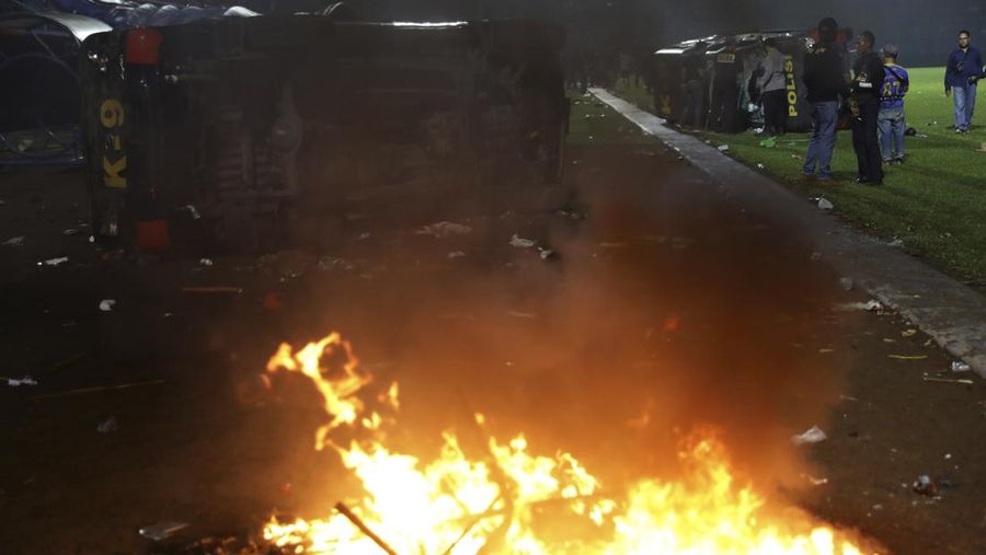 Plain-clothed officers stand near the wreckage of police vehicles damaged during a clash between supporters of two Indonesian soccer teams at Kanjuruhan Stadium in Malang, East Java, Indonesia, Saturday, Oct. 1, 2022. Panic following police actions left over 100 dead, mostly trampled to death, police said Sunday. (AP Photo/Yudha Prabowo)