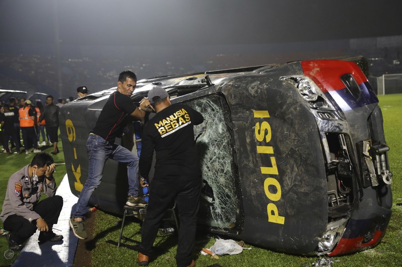 Indonesia Soccer Deaths Plain-clothed officers stand near the wreckage of police vehicles damaged during a clash between supporters of two Indonesian soccer teams at Kanjuruhan Stadium in Malang, East Java, Indonesia, Saturday, Oct. 1, 2022. Panic following police actions left over 100 dead, mostly trampled to death, police said Sunday. (AP Photo/Yudha Prabowo)