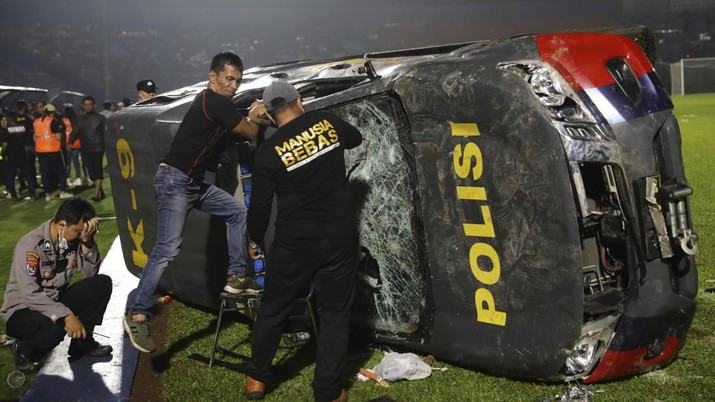 Officers examine a damaged police vehicle following a clash between supporters of two Indonesian soccer teams at Kanjuruhan Stadium in Malang, East Java, Indonesia, Saturday, Oct. 1, 2022. Panic following police actions left over 100 dead, mostly trampled to death, police said Sunday. (AP Photo/Yudha Prabowo)