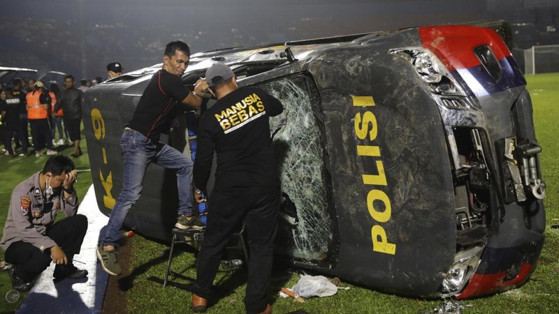 Plain-clothed officers stand near the wreckage of police vehicles damaged during a clash between supporters of two Indonesian soccer teams at Kanjuruhan Stadium in Malang, East Java, Indonesia, Saturday, Oct. 1, 2022. Panic following police actions left over 100 dead, mostly trampled to death, police said Sunday. (AP Photo/Yudha Prabowo)