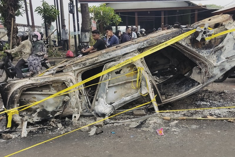 Indonesia Soccer Deaths Plain-clothed officers stand near the wreckage of police vehicles damaged during a clash between supporters of two Indonesian soccer teams at Kanjuruhan Stadium in Malang, East Java, Indonesia, Saturday, Oct. 1, 2022. Panic following police actions left over 100 dead, mostly trampled to death, police said Sunday. (AP Photo/Yudha Prabowo)