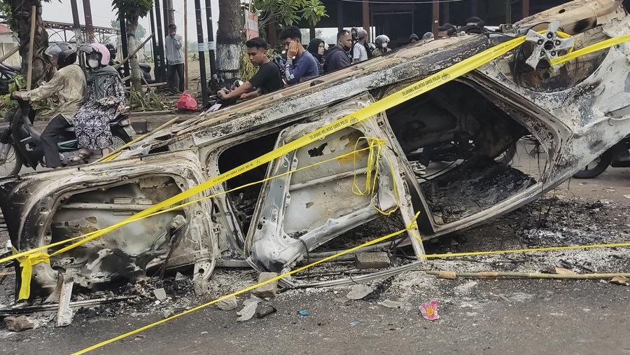 Plain-clothed officers stand near the wreckage of police vehicles damaged during a clash between supporters of two Indonesian soccer teams at Kanjuruhan Stadium in Malang, East Java, Indonesia, Saturday, Oct. 1, 2022. Panic following police actions left over 100 dead, mostly trampled to death, police said Sunday. (AP Photo/Yudha Prabowo)