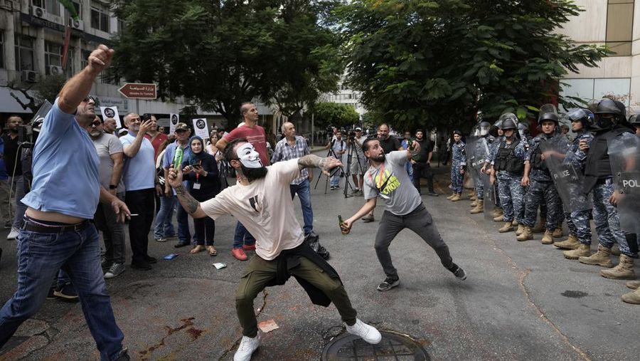 Protesters throw bottles glasses at the Lebanese Central Bank building, background, where the anti-government demonstrators rally against the Lebanese Central Bank Governor Riad Salameh and the deepening financial crisis, in Beirut, Lebanon, Wednesday, Oct. 5, 2022. (AP Photo/Hassan Ammar)
