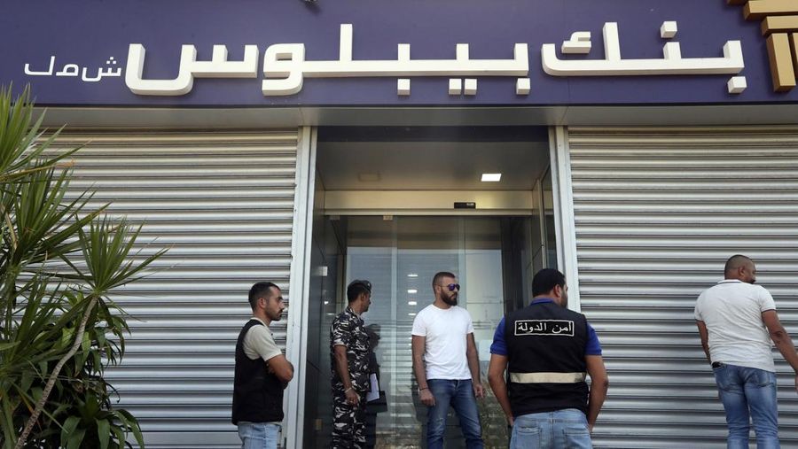 Lebanese security officers stand at the entrance of a Byblos Bank branch that was broken into by depositor Ali Hodroj holding a handgun, firing a warning shot and demanding about $40,000 of his trapped savings, in Tyre, south Lebanon, Tuesday, Oct. 4, 2022. Hodroj retrieved about $9,000 in Lebanese pounds following negotiations before he turned himself in to police outside the branch. Lebanese depositors, including a retired police officer, stormed at least four banks in the cash-strapped country Tuesday after banks ended a weeklong closure and partially reopened. (AP Photo/Mohammed Zaatari)