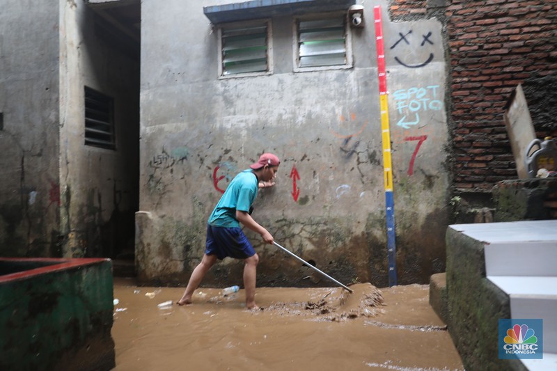 Warga menyapu sisa lumpur usai banjir di kawasan Bidara Cina, Jatinegara, Senin (10/10). (CNBC Indonesia/Muhammad Sabki)