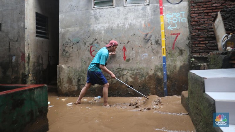 Warga menyapu sisa lumpur usai banjir di kawasan Bidara Cina, Jatinegara, Senin (10/10). (CNBC Indonesia/Muhammad Sabki)