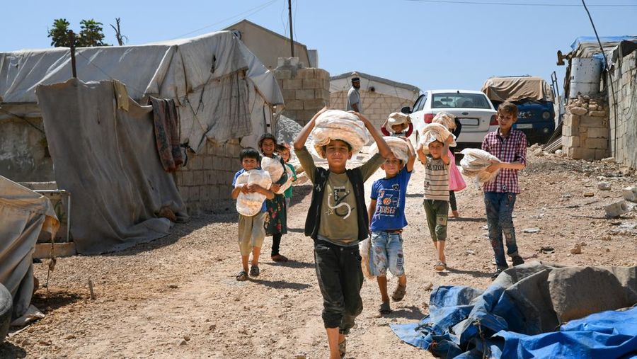 Anak-anak menerima roti yang dibagikan oleh organisasi bantuan di kamp-kamp pengungsi di Aqrabat di pedesaan Idlib, barat laut Suriah, Idlib, pada 28 Agustus 2022. (Photo by Rami Alsayed/NurPhoto via Getty Images)