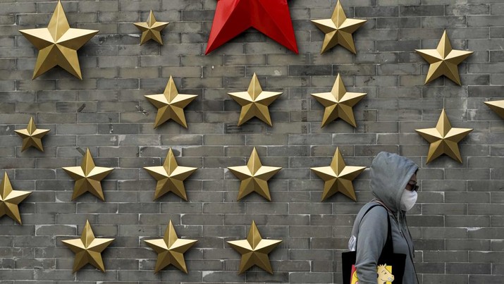 Seorang wanita mengenakan masker berjalan didepan simbol komunis dari sebuah bintang yang dipajang di luar sebuah restoran di Beijing, Minggu (9/10/2022). Partai Komunis China (PKC) bakal menyelenggarakan kongres lima tahunan mereka yang ke-20 pada 16 Oktober mendatang. (AP Photo/Andy Wong)
