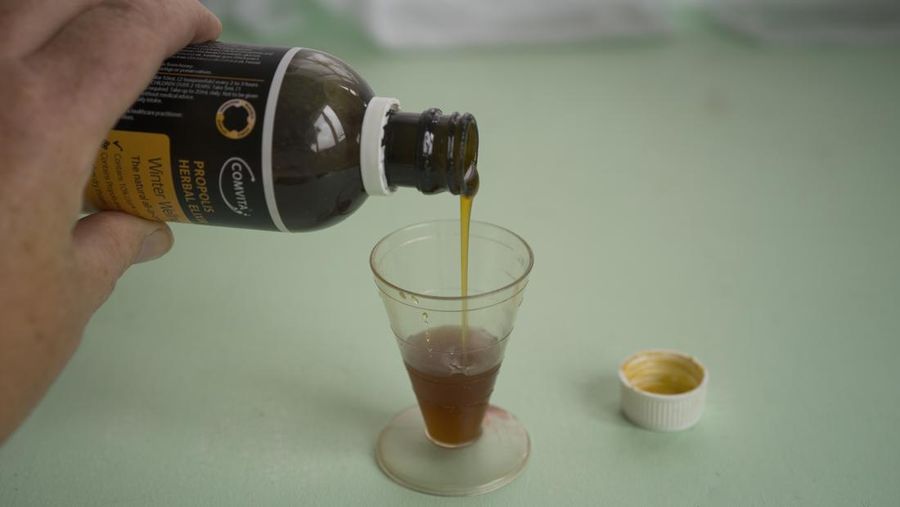 Propolis, Manuka honey and echinacea herbal elixir which helps relieve cold symptoms being poured into a measuring cup.